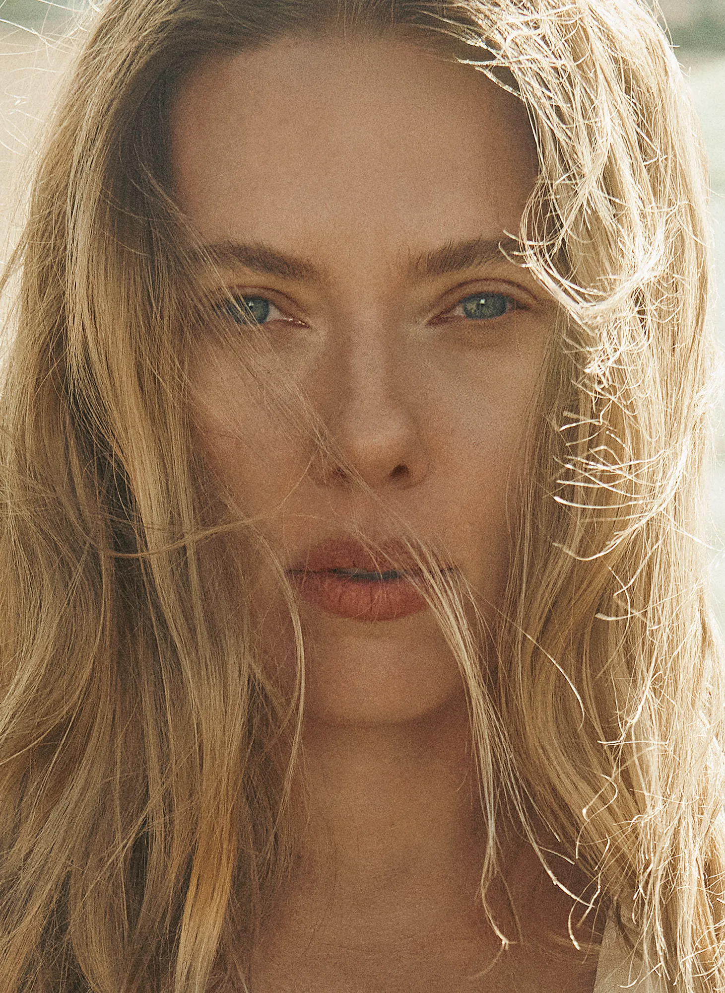 Close-up portrait of Scarlett Johansson with natural makeup and windswept hair, gazing into the camera on the beach.