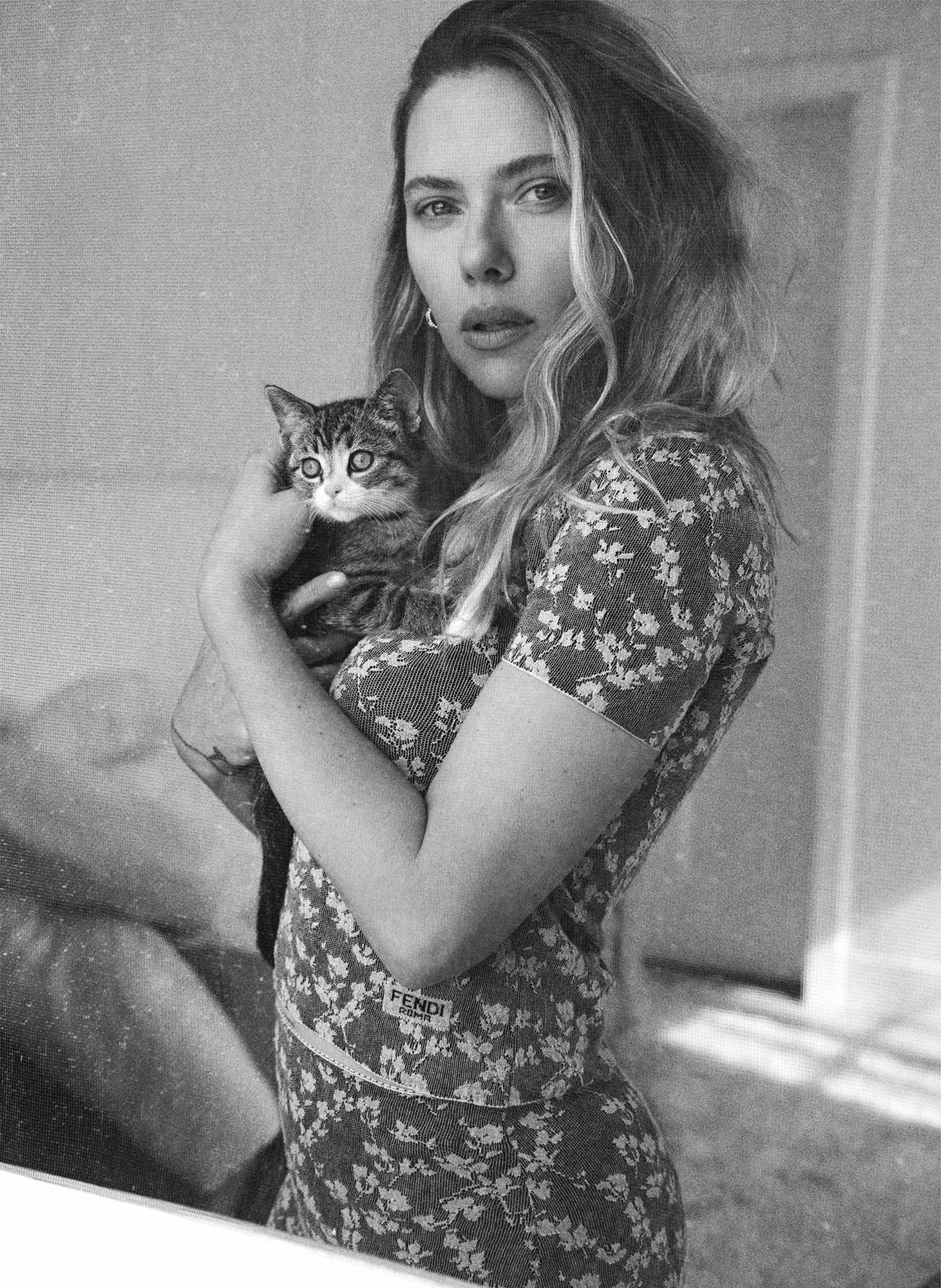Scarlett Johansson holding a kitten in her arms while wearing a floral Fendi top, captured in a black and white mirror portrait.