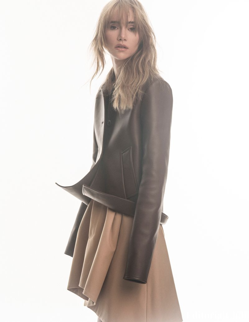 Suki Waterhouse posing in structured leather jacket and beige skirt with backlit white background – Elle Spain March 2025