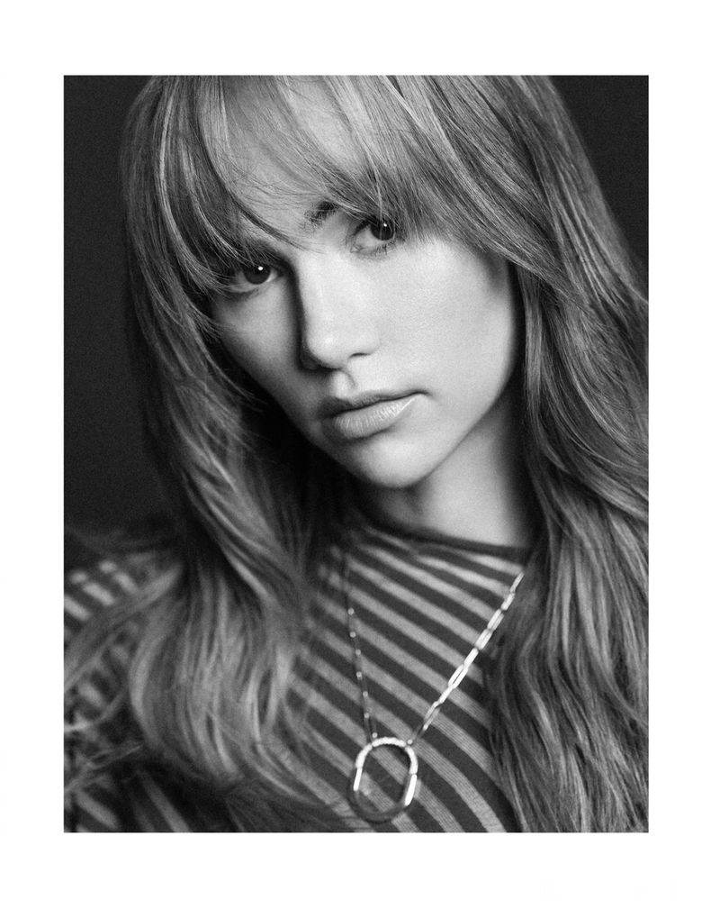 Monochrome portrait of Suki Waterhouse wearing a striped top and a statement chain necklace, softly lit with a pensive expression.