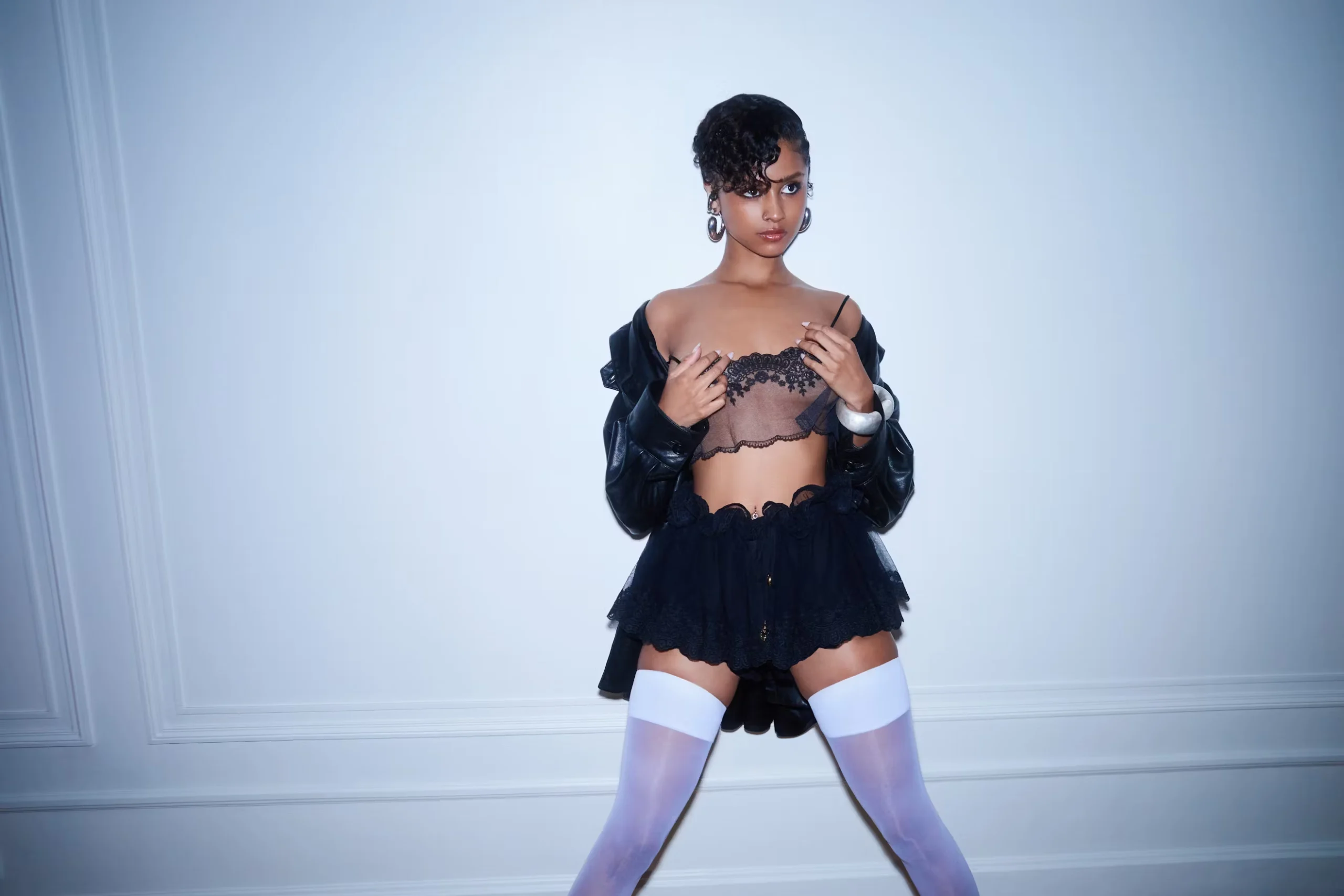 Tyla poses confidently in a black lace bralette, leather jacket, and mini skirt with white thigh-high stockings for Nylon Magazine April 2025 editorial shoot.
