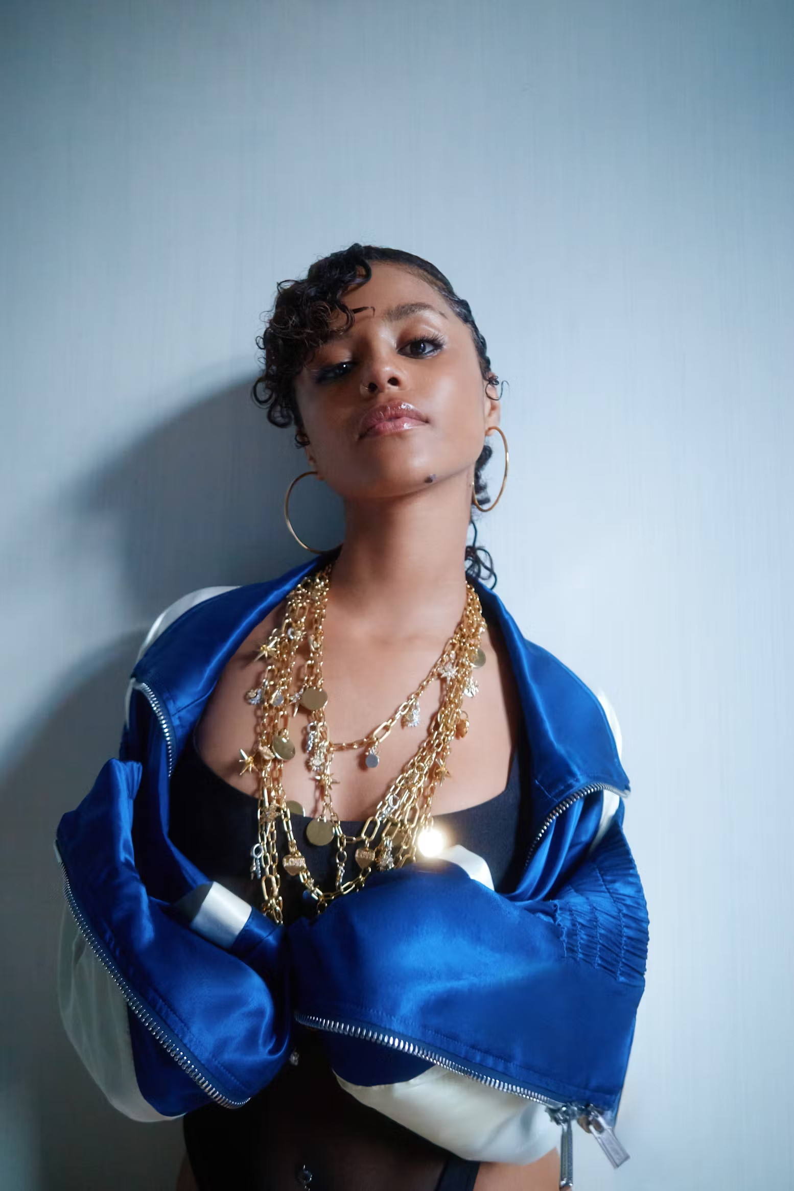 Portrait of Tyla in a royal blue track jacket and stacked gold necklaces, exuding bold energy in Nylon Magazine April 2025 close-up fashion shot.